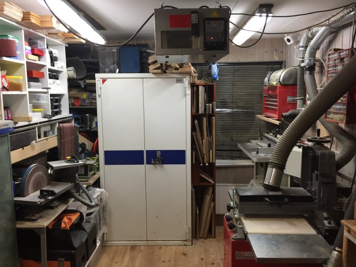 Verkstadsrum med överfulla arbetsbänkar och flera slipmaskiner, omgivna av verktyg och material.