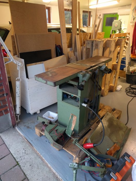 En äldre modell hyvelmaskin i ett rörigt garage, redo för underhåll och reparationer.
