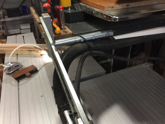 Sågskydd monterat på en såg med synliga klyvkniv och rörsystem i en verkstad.