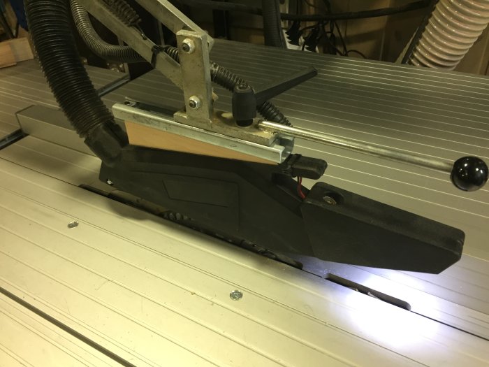 Modifierat sågskydd monterat på klyvkniv vid såg med dammsugaranslutning och handhjul.