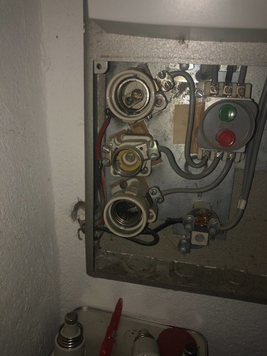 Inuti en elcentral med gamla säkringshållare, sliten huvudbrytare och en skadad kabel med bränt hölje.