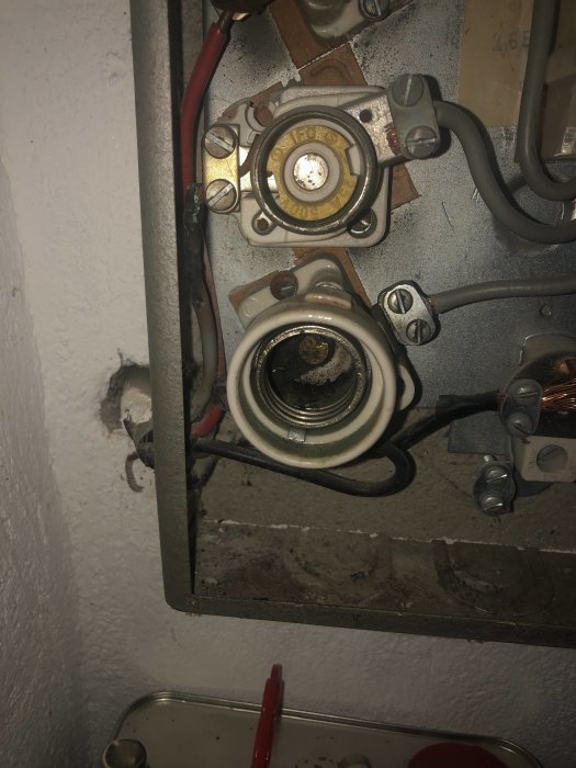 Gamla säkringar i elskåp med bränt kabelhölje och synliga ledningar.