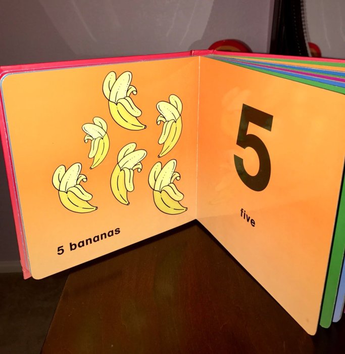 Öppen barnbok visar fem bananer och siffran 5 med texten "5 bananas" "five".