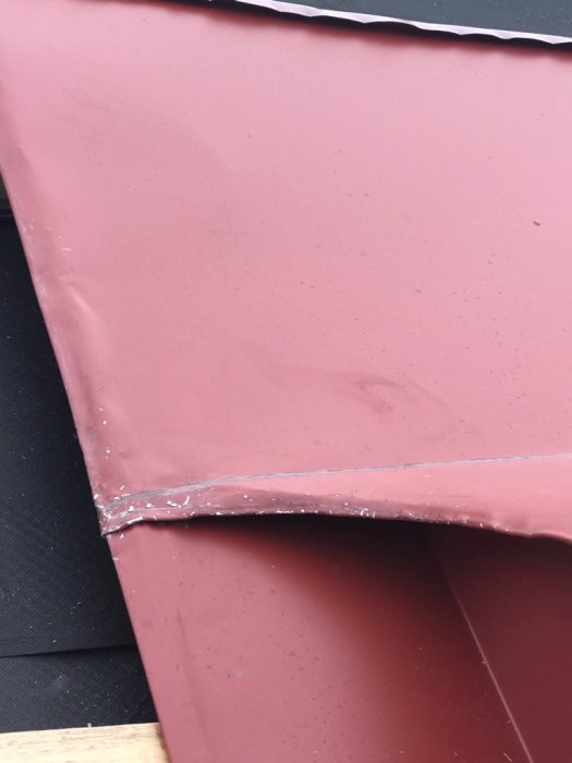 Skadad och repad röd plåt med tydliga defekter och vattenskador, indikerar dåligt hantverk under takbyte.