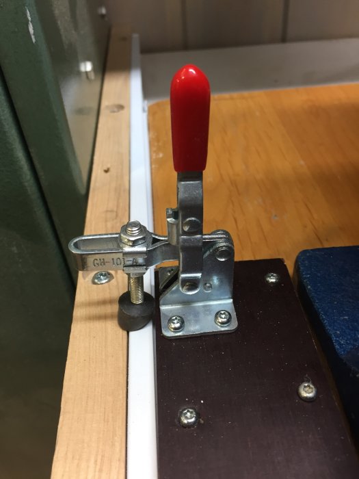 Metallspännare monterad på träskiva för att låsa utdragsskivor på en arbetsbänk.