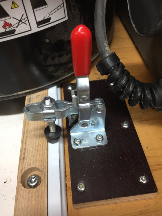 Monterad spännare med röd handtagsspak fastsatt på en arbetsbänk för att låsa utdragsskivor.