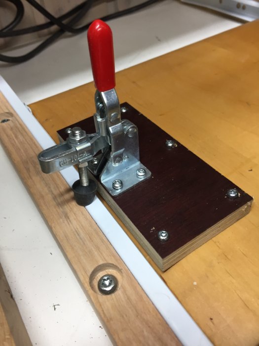 Ett spännareverktyg fastmonterat på en träskiva, använt för att låsa utdragsskivor på en arbetsbänk.