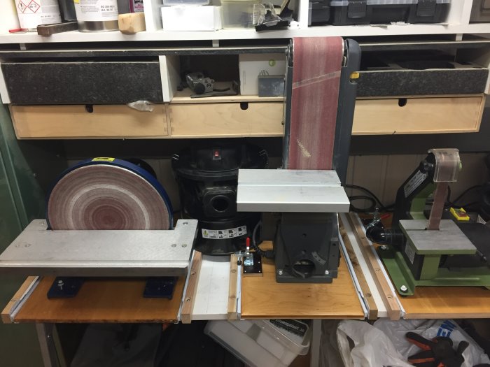 Verkstadsutrymme med utdragsskivor, slipmaskiner och verktyg ordnade på en arbetsbänk.