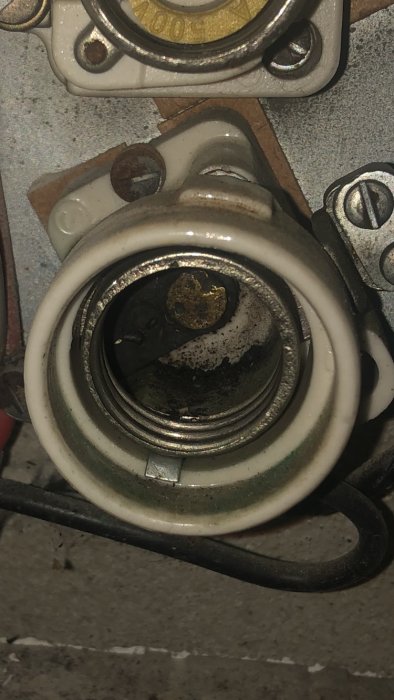 Öppen säkringshållare på en vägg med eventuella rester i botten och en svart ledning kopplad till sidan.