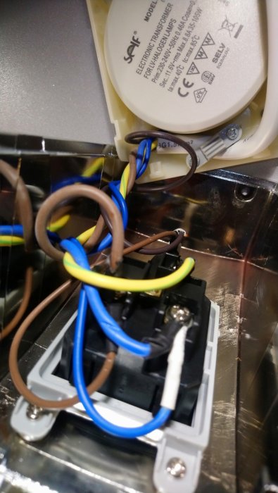 Öppnat elektroniskt halogenlampetransformatorlock med synliga kablar och anslutningar, utan tecken på brännskador.