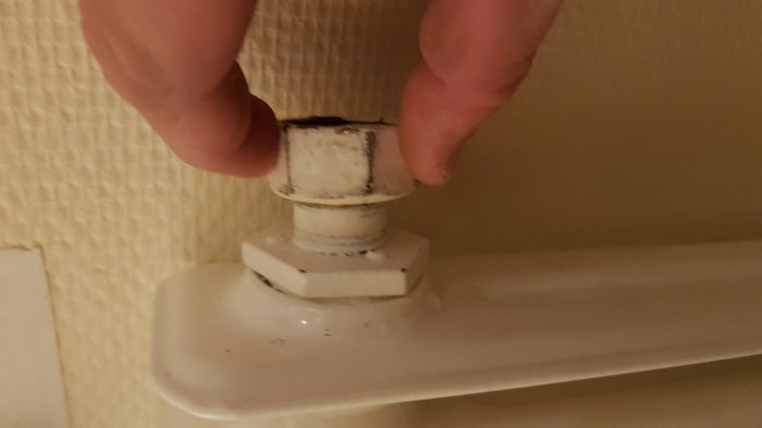 Hand som håller en sektionsradiatoranslutning med skador och repor, indikerande problem med tätning.