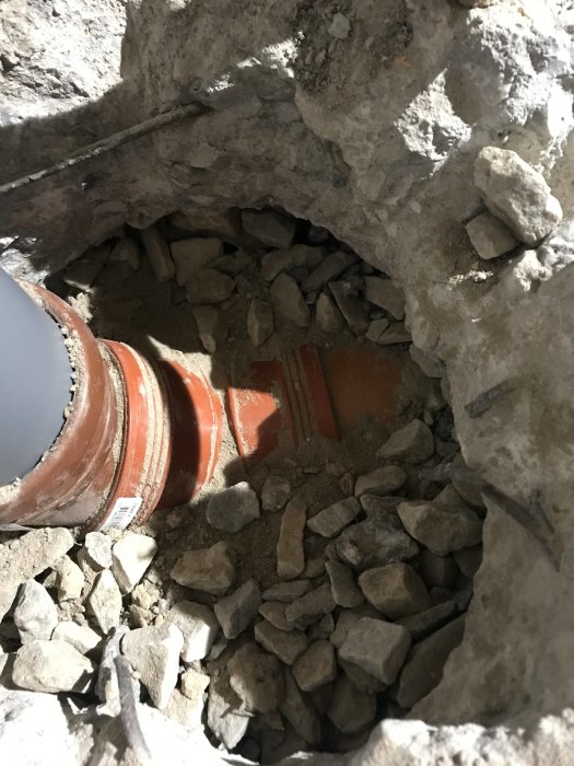 Uppgrävd betong och sten runt en brun avloppsröranslutning som ligger på en sandbädd.