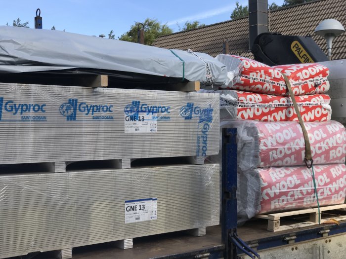 Leverans av byggmaterial: gipsskivor och isoleringsbalar redo för renoveringsprojekt.