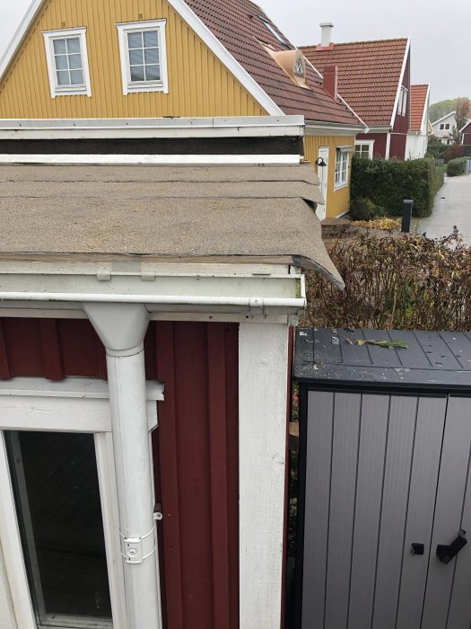 Första lagret av takpapp på förrådstaket framför ett gult hus med detaljbild på kanten.