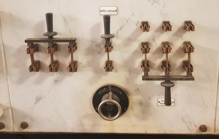 Gammal kontrolltavla i marmor med brytare och rattar för elektrisk styrning, inklusive svastika-symbol.
