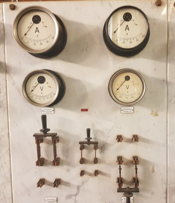 Historisk kontrolltavla med mätinstrument och brytarsystem monterade på marmorskiva från tidigt 1900-tal.