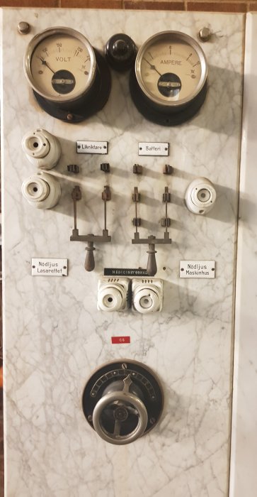 Gammal kontrolltavla i marmor med mätinstrument, vred och skyltar för elektrisk anläggning.