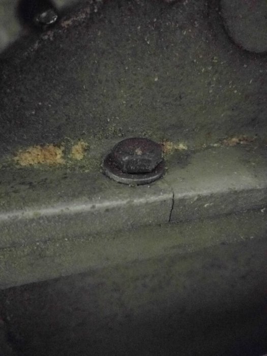 Närbild på en sprucken infästningspunkt och rostig bult på maskinens gavel.