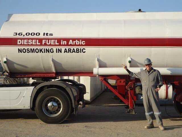 Arbetare i skyddshjälm och arbetskläder står bredvid en stor tankbil med texten "DIESEL FUEL in Arabic".