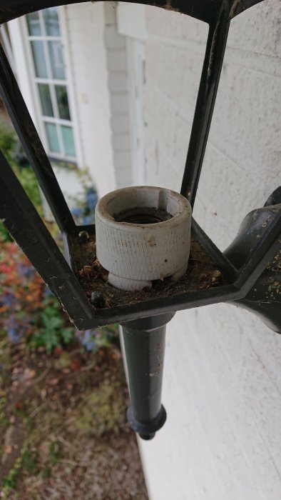 Smutsig lamphållare monterad på en utomhuslampa nära en vit vägg, behöver rengöras.