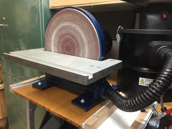 Verkstad med slipmaskin fastskruvad på bänk och ansluten till dammsugaranordning.