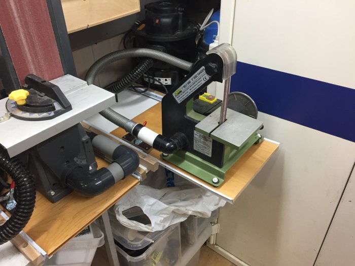 Verkstadsbänk med fastskruvade slipmaskiner och dammsugarslangar anslutna.