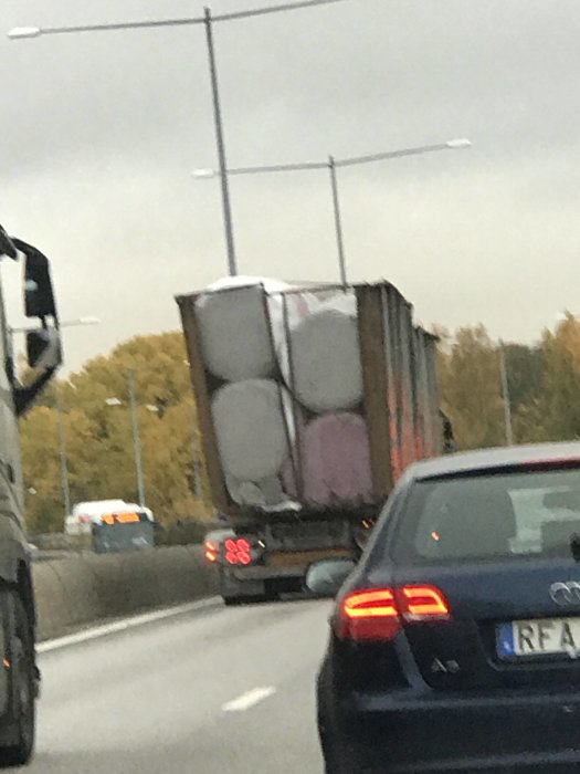 Lastbil med lutande lastavdelning ser ut att köra snabbt på en motorväg.