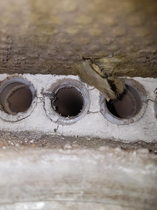 Bild på fördelningslådan i ett ventilationssystem med flera 25mm hål i betongen där plast rör görs fast.
