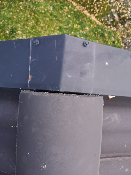 Taknock med en glipa mellan vindplåt och nockpanna, synliga spikar och underliggande takpapp.