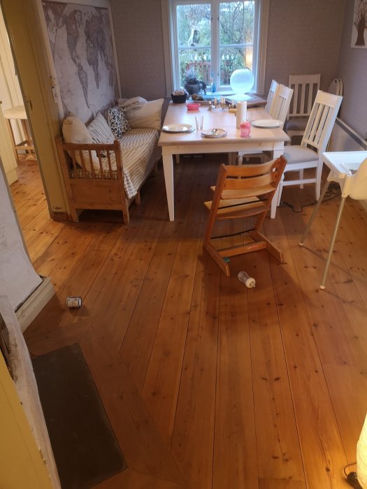 Matsal med gammalt trägolv och upplagda möbler inklusive bord, stolar och en soffa, med fokus på golvet.