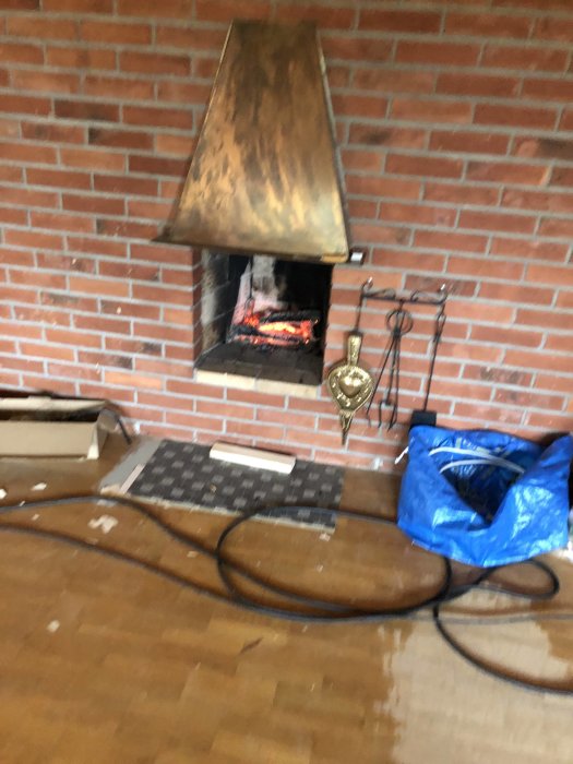 Öppen tegelspis med brinnande eld, eldstadsredskap, och rör på golvet i ett renoveringsprojekt.