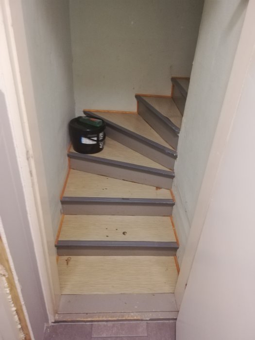 Trappa under renovering med delvis målade steg och en färgburk på ett trappsteg.