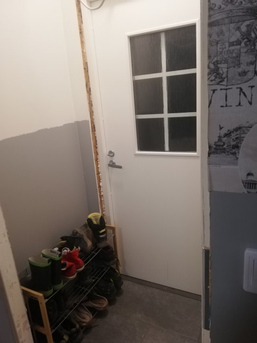 Renoveringsprojekt av rum med en dörr med frostglas, skohylla med skor och oslipade väggar.