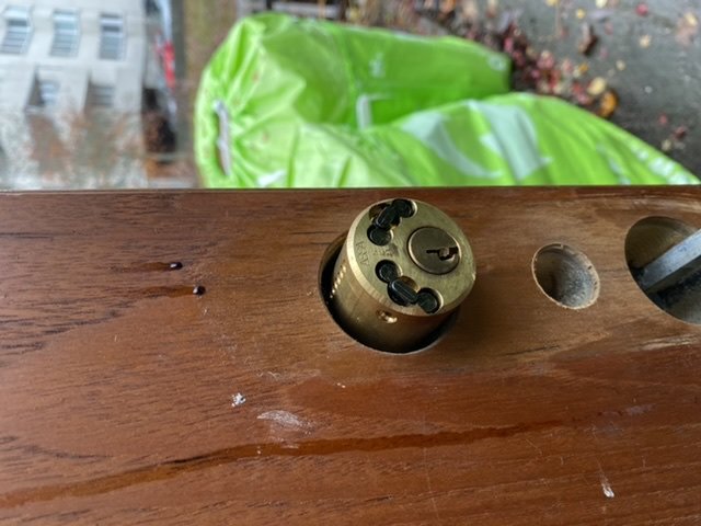 Närbild av en fastsatt rund dörrlåscylinder i en träyta med en till synes förvirrad användare.