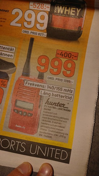 Handhållen jaktradio med antenn och frekvensdisplay, reklam i tidning med prisinformation.