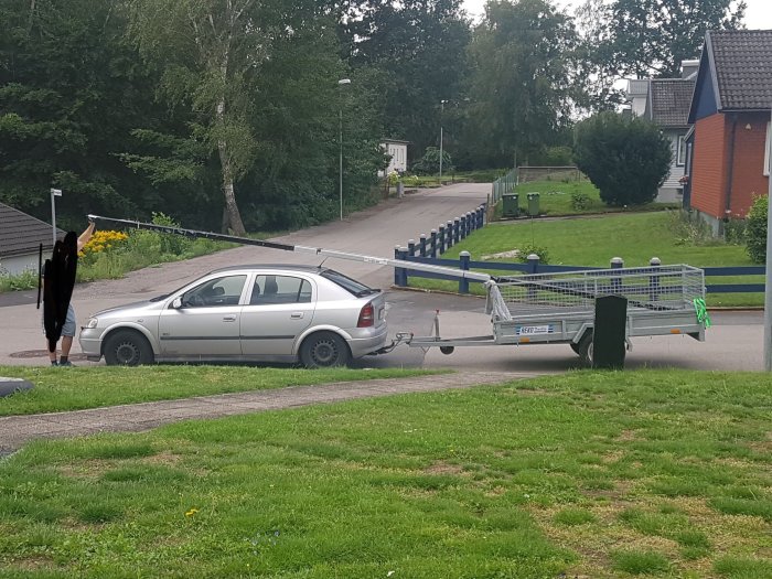 Bil parkerad med en lång byggställningsdel ovanpå fastspänd på köpkärra, troligen orsakar balansproblem.