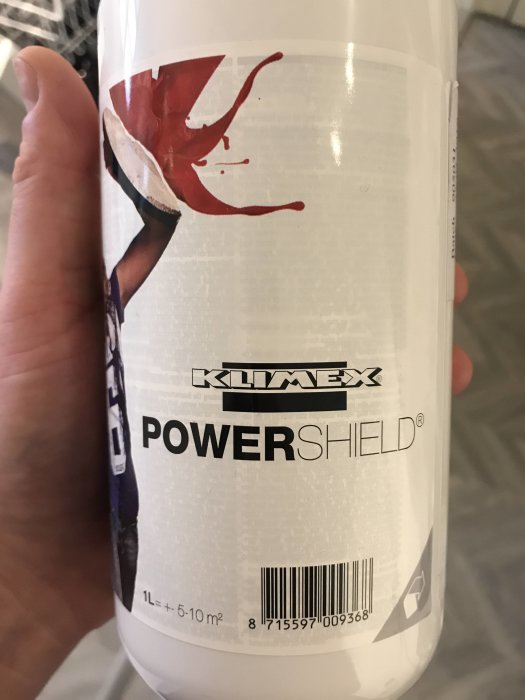 Hand håller en behållare med texten "KLIMEX POWERSHIELD" och en bild av en stänkande vätska.