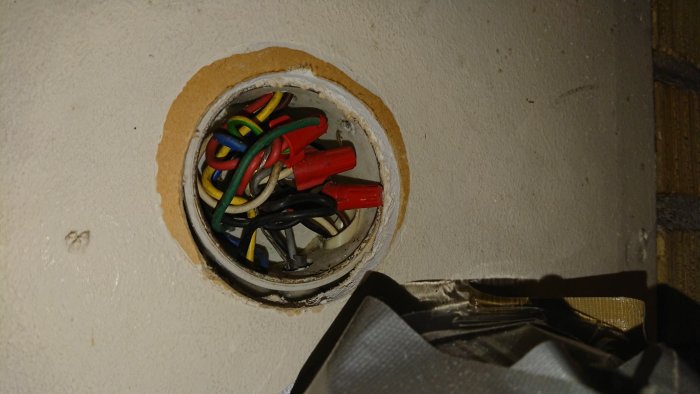 Elektrisk dosa med rörigt hopkopplade kablar och ståltråd som går in i väggen.