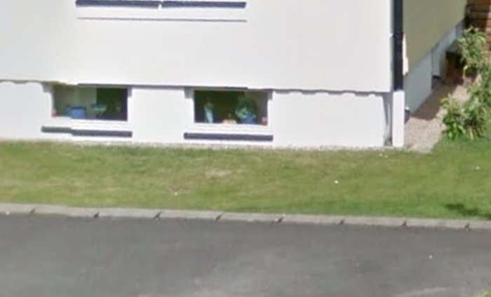 Ljusa källarfönster på husfasad vid en sluttning, med gata och trottoar i förgrunden.