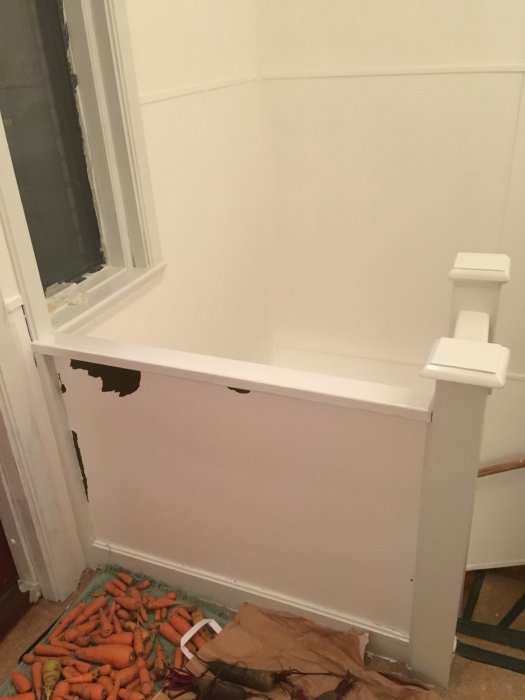 Vitt trappräcke i behov av höjning intill en vit vägg och fönster, med morötter på golvet.