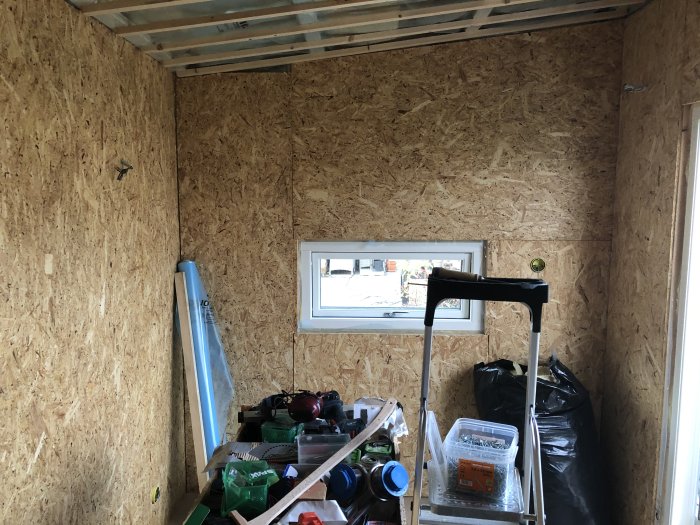En vägg täckt med OSB-skivor i ett rum under renovering med verktyg och byggmaterial.