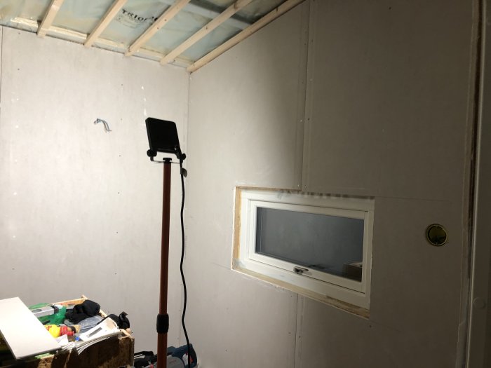 Renoverat rum med nymonterade gipsskivor på väggen och ett litet fönster.