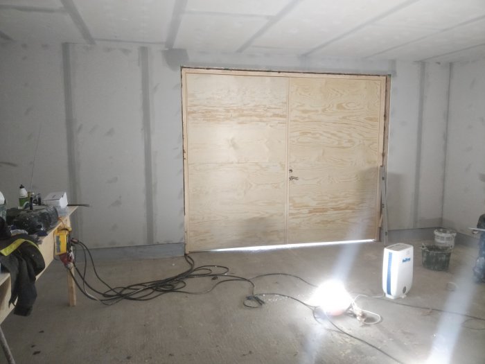 Nyinstallerad port i ett ofärdigt garage med spacklade väggar och verktyg på golvet.