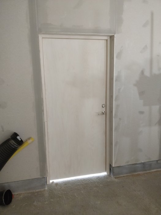 Ommålad dörr monterad i en spacklad vägg med synliga tätningsskikt vid golvet i ett garage.