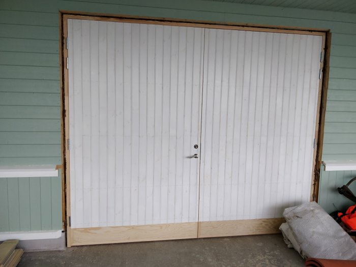 Nymonterad vit dörr och port i ett garage, omgiven av träramar väntande på tätning och målning.