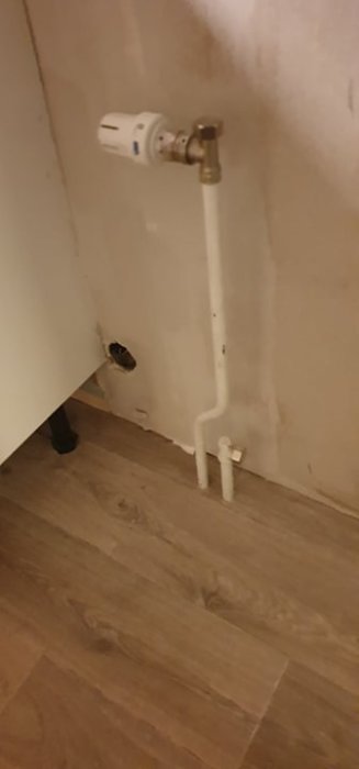 Radiatoranslutning i hörn av rum med vita rör på trägolv som behöver passa nya radiatorer.