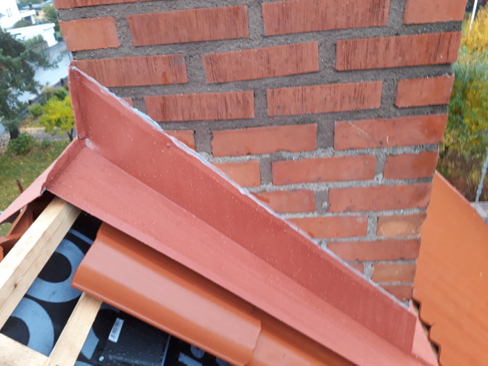 Skarv mellan takpannor och tegelvägg, oavslutat takläggningsarbete med synlig takpapp och råspont.