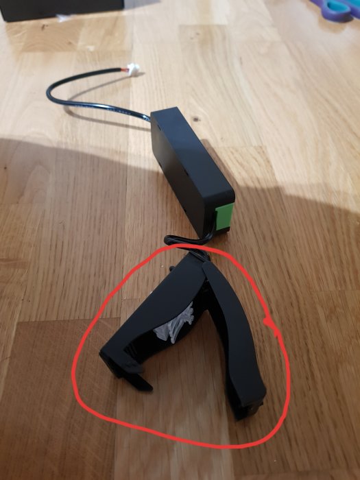 Svart transformator med kabel och en kopplingsdosa markerad med rött på ett trägolv.