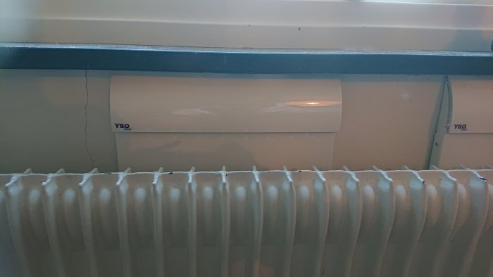 Vägg med spricka över element och ventilationsgaller, indikerar möjligt byggfel.