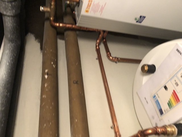 Kopparrör i en VVS-installation, ett rör ansluter till en pump och ett till element, intill en energimärkt enhet.